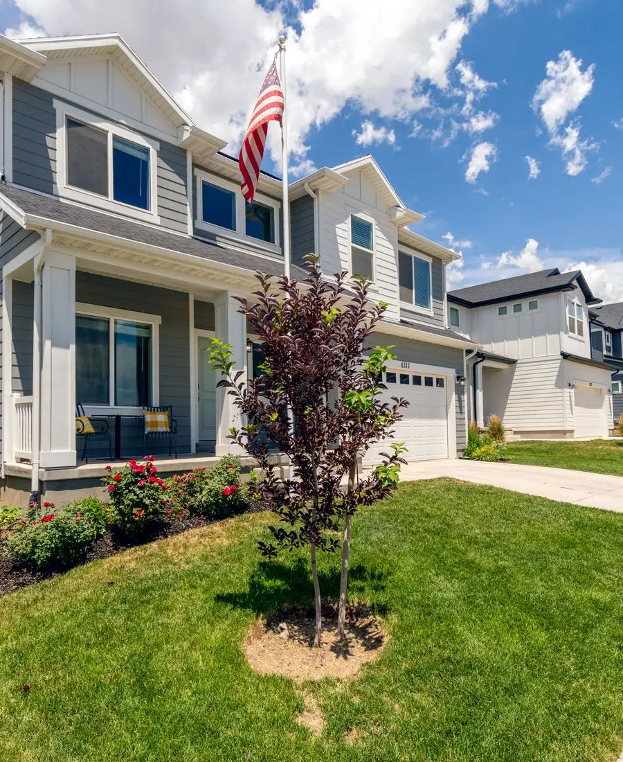 Two-story suburban rental home with white and gray siding, front porch and landscaped garden
