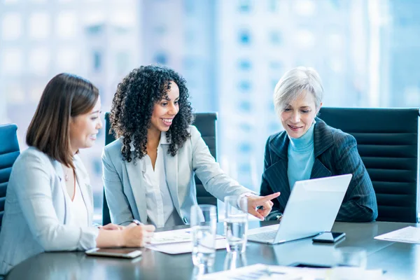 Three women in business attire reviewing property investment documents and laptops in a high-rise office